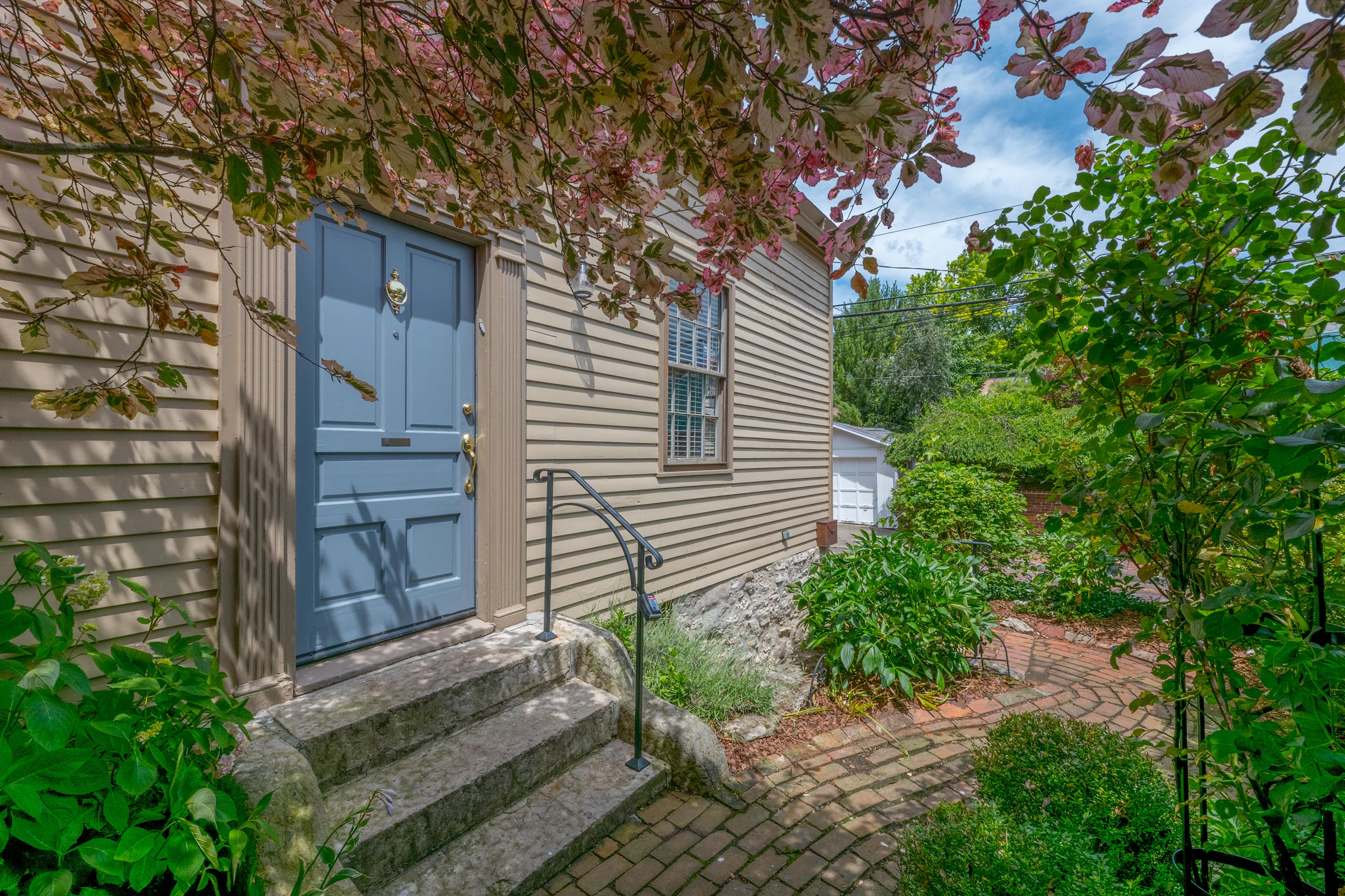 The side entrance, framed by a flowering tree and garden plantings.